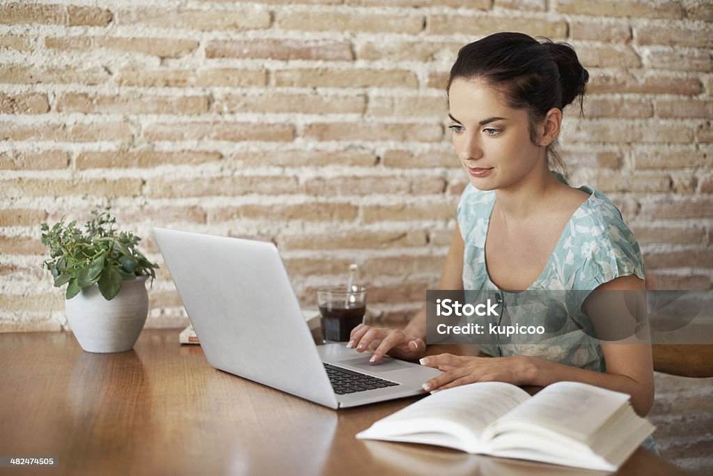 Using the tools at her disposal An attractive young woman doing some research using her laptop and text book 20-29 Years Stock Photo