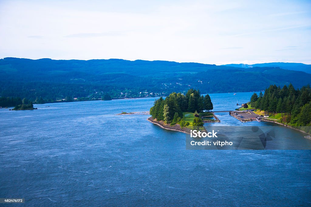 Green island blue water Columbia River scenic Columbia Gorge Green island covered with trees on the Columbia River in the scenic Columbia Gorge conservation area in the middle of blue water of the broad river footbridge connected with the right bank. The perfect place to relax, travel, fishing or hiking in Oregon. 2015 Stock Photo