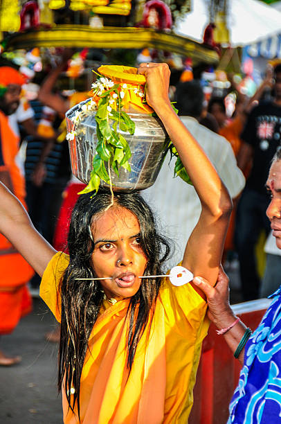 Kuala Lumpur, Malaysia - January 17, 2014: Pierced devotee carrying pot of milk, the simplest type of kavadi, offers to god. A local is holding the devotee from falling while other locals are celebrating the festival along the way.