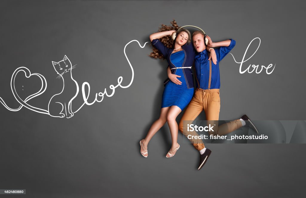 Song about love. Happy valentines love story concept of a romantic couple sharing headphones and listening to the music about love against chalk drawings background of lyrics. 2015 Stock Photo