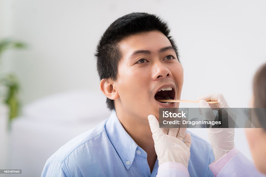 Throat examination Doctor examining throat of patient with tongue depressor Tongue Depressor Stock Photo