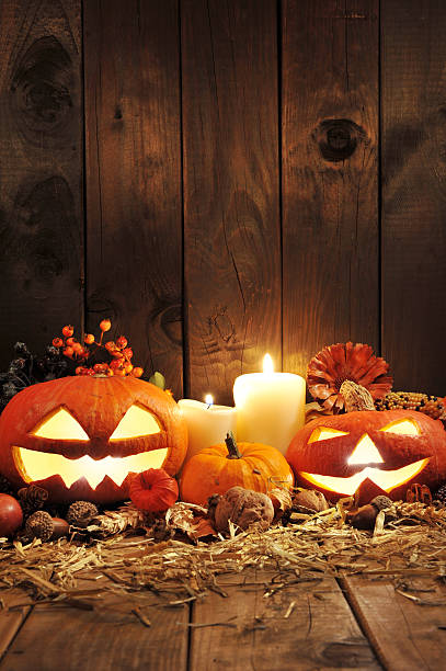 halloween pumpkins illuminated halloween pumpkins, candles, nuts, maize-cob and apple on straw in front of old weathered wooden board in candlelight chinese lantern lily photos stock pictures, royalty-free photos & images