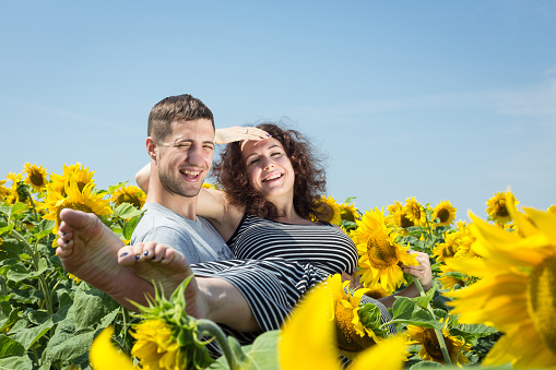 Man is holding woman in his arms. Sweethearts in the field with sunflowers.