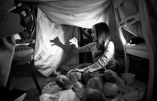 Black and white photo of cute girl making shadow of dog with hands and flashlight