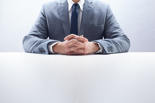 Businessman sitting by the desk with hands folded.