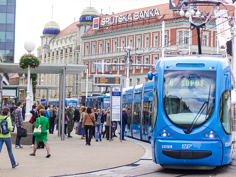 Zagreb, Сroacia - September 22, 2014: Streetcar station in the Zagreb central square Ban Jelacic. A blue Tram is just living the station, while a lot of people wait at station for next tram. In background are houses with lot of commercial panels. It is grey autumn day.