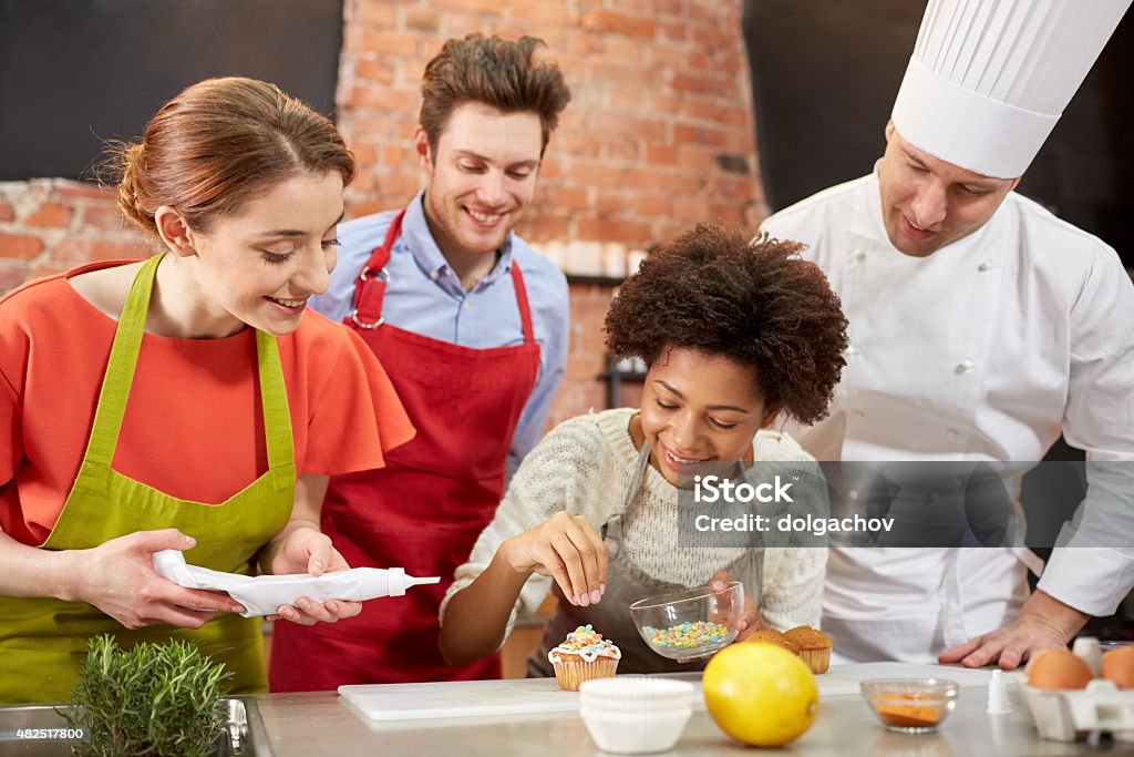 happy friends and chef cook baking in kitchen cooking class, culinary, bakery, food and people concept - happy group of friends and male chef cook baking in kitchen Baking Stock Photo