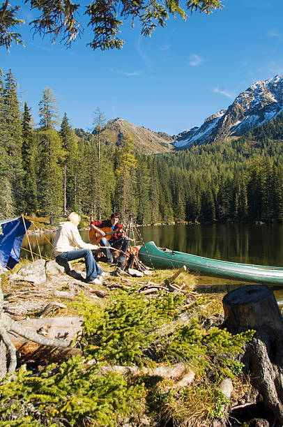 istock Young couple camping by lake, man playing guitar 482524898