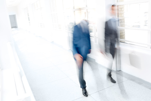 Blurred image of two businessmen walking along corridor