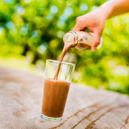 A person pouring chocolate milkshake from bottle into a glass