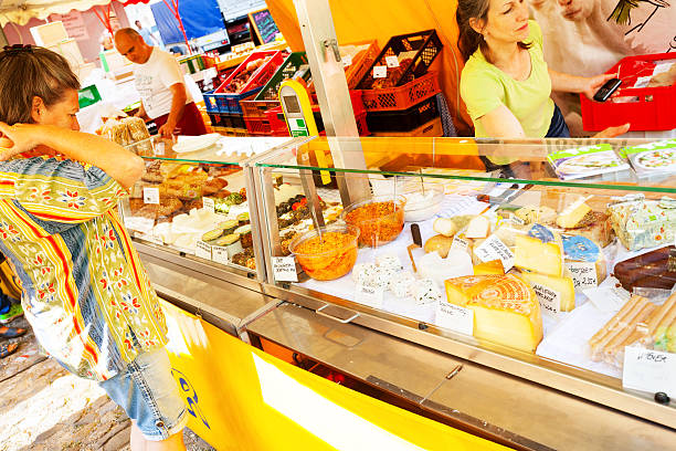 Lindau, Germany - July 11, 2015: Summertime scene on local market in Lindau (island). A caucasian woman is byuing cheese at market stall. A male and a female vendor are serving customers.