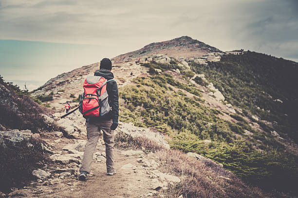 Woman Hiker wearing a backpack walking to the Mountain Summit. Taken at Franconia Ridge trail in New Hampshire, Usa. A retro filter and grain added in post process.