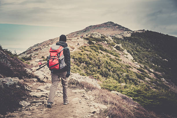 Woman Hiker Walking to the Mountain Summit Woman Hiker wearing a backpack walking to the Mountain Summit. Taken at Franconia Ridge trail in New Hampshire, Usa. A retro filter and grain added in post process. franconia new hampshire stock pictures, royalty-free photos & images