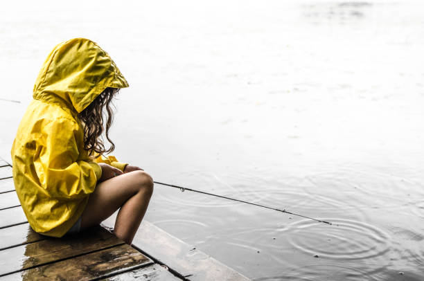 Blonde mother and three year old daughter in denim shorts with belts with red bows eat watermelon and fish on a pier on the river