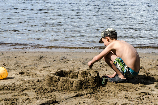 Boy building a sand castle on the beach of lake Sept-Iles (Portneuf) at summer camp.