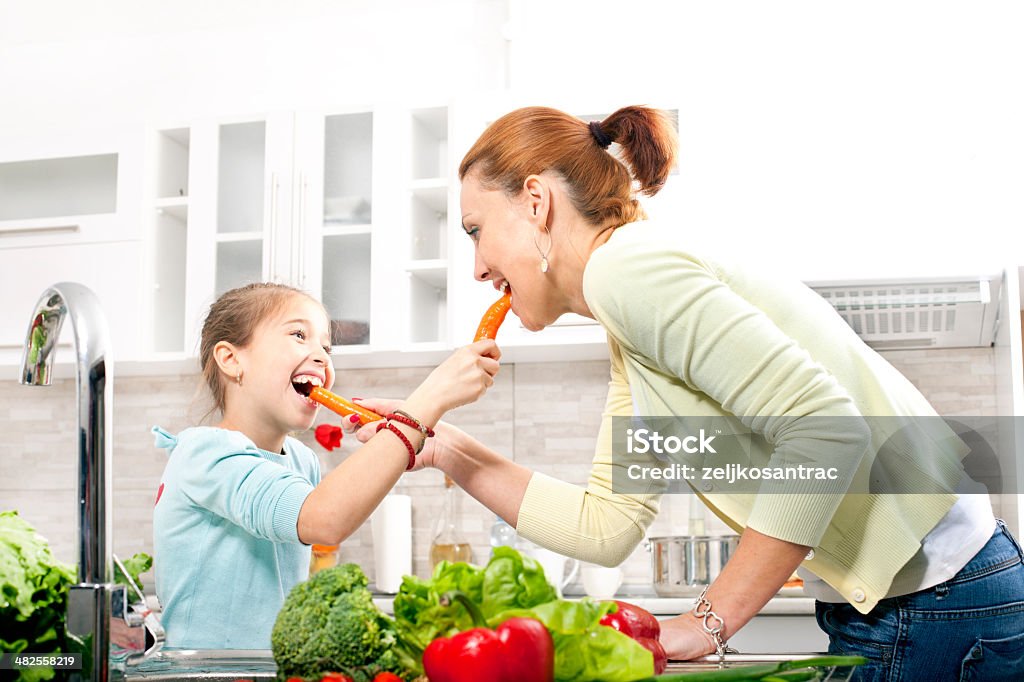 Junge Frau und kleines Mädchen Essen Karotten in der Küche - Lizenzfrei Beißen Stock-Foto
