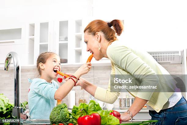 Junge Frau Und Kleines Mädchen Essen Karotten In Der Küche Stockfoto und mehr Bilder von Beißen