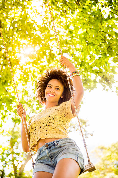 A young stylish woman in a summer look rides on a swing on a pink isolated background. Studio photo. Summer concert.