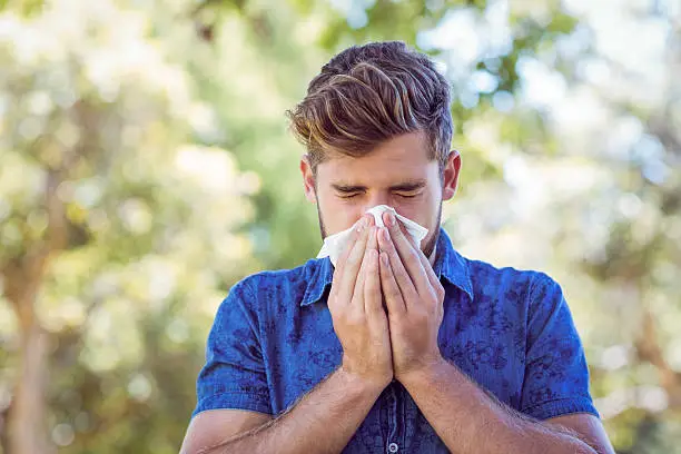 Handsome hipster blowing his nose on a sunny day