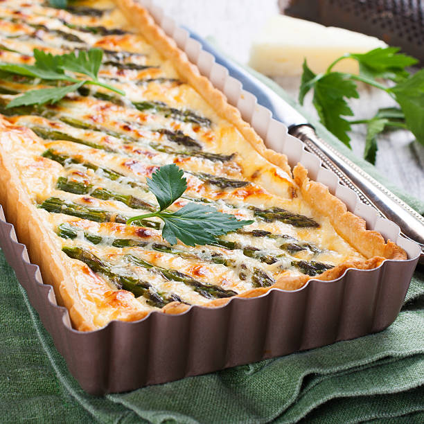 Rectangle-shaped grilled asparagus savory tart with pecorino and bacon next to a french cutting knife on a rustic wooden background