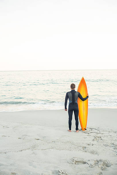 istock Man in wetsuit with a surfboard at beach 482566346