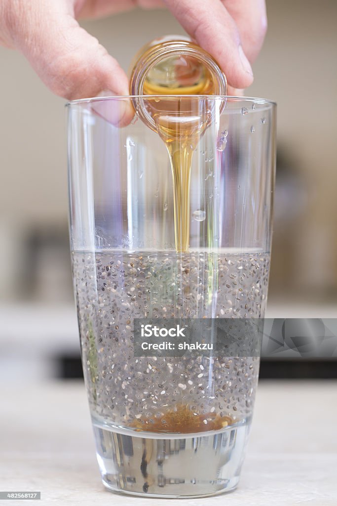 Chia beverage Closeup of hand pouring small jar of honey into clear glass beverage of water and chia seeds Honey Stock Photo