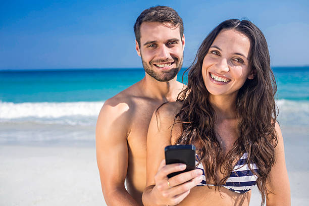 istock Smiling couple using smartphone at the beach 482574104