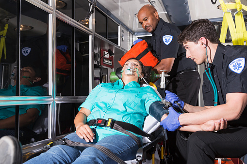 Multi-ethnic paramedics with Hispanic woman on stretcher, inside ambulance. 