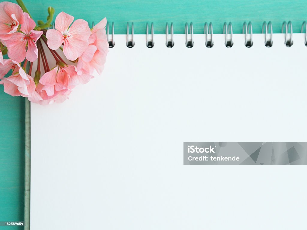 Paper with a flower White empty page of an open notebook with a geranium flower put on green pastel wooden table 2015 Stock Photo