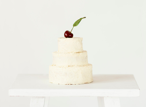 White small cake on three floors decorated  fresh cherry on top. Cake covers white  background.