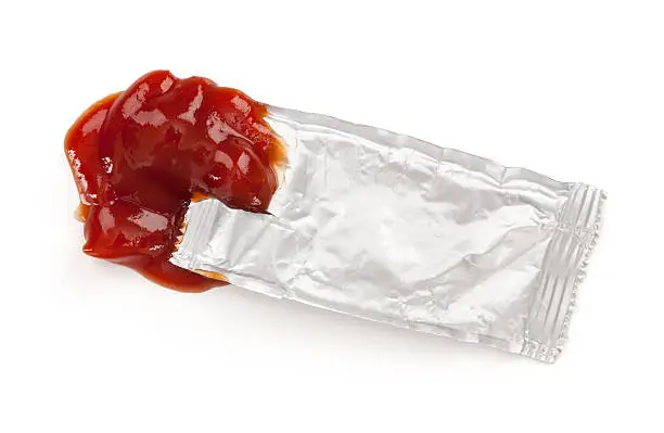 Open ketchup packet, isolated on white.