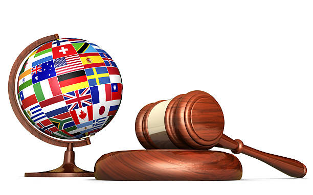 International law systems, justice, human rights and global business education concept with world flags on a school globe and a gavel on a desk isolated on white background.