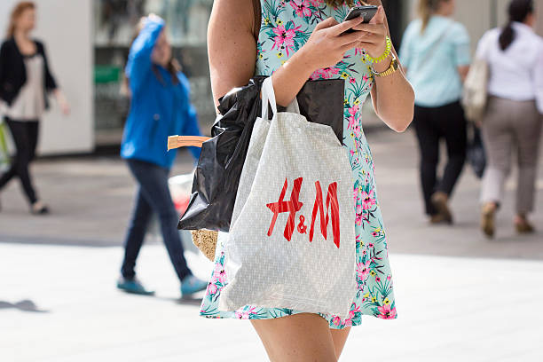 Hennes and Mauritz plastic bag shopping street sale Wiesbaden, Germany - July 28, 2015: An unrecognisable female pedestrian with a plastic bag of Hennes and Mauritz  walking by in a shopping street in the city center of Wiesbaden. H and M (full name: Hennes and Mauritz) is a Swedish retail-clothing company. h and m stock pictures, royalty-free photos & images