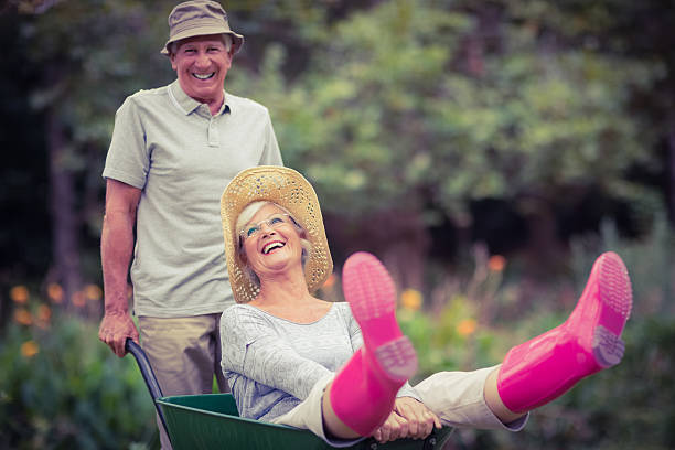 felice coppia senior giocando con una carriola - gardening couple senior adult ethnic foto e immagini stock