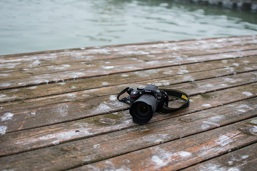 Subotica, Serbia - July 28th, 2015: Nikon D5200 camera with 18-105mm lens standing on wooden boards. Photographed on lake dock, on a very foggy morning. The time was around 6 a.m.Photo was taken also with Nikon.