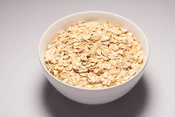 istock Raw oatmeal flakes in white ceramic bowl on white background 482606296