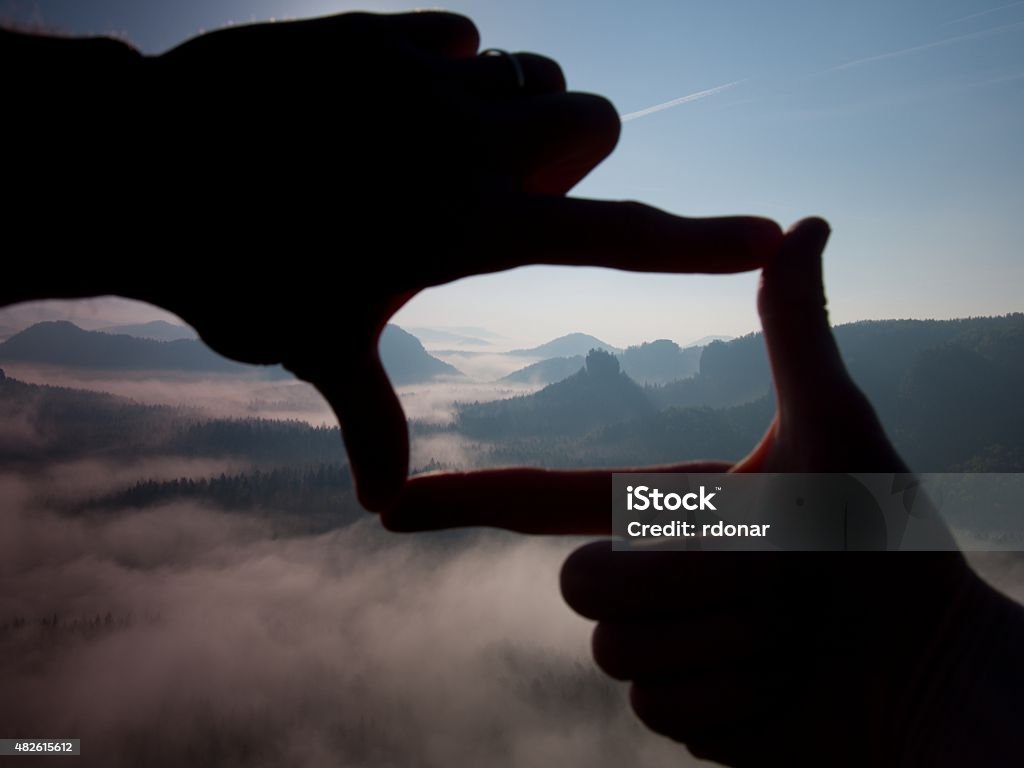 Fingers frame. Close up of hands making frame gesture. Close up of hands making frame gesture. Blue misty valley bellow rocky peak. Sunny spring daybreak in rocky mountains.Close up of hands making frame gesture. Blue misty valley bellow rocky peak. Sunny spring daybreak in rocky mountains. 2015 Stock Photo