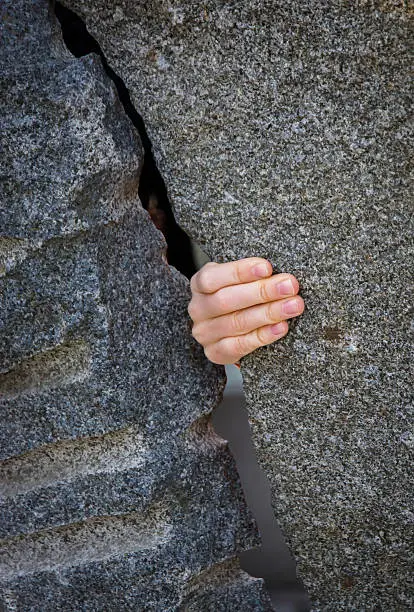 Children´s hand exploring space through a gap between two stone walls