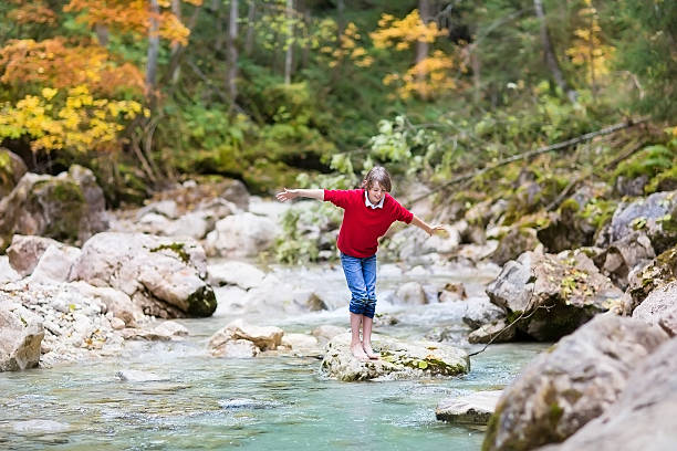 istock Smiling happy boy crossing wild mountain river jumping on stones 482619351