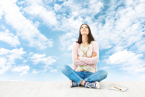 Girl teenager thinking inspiration or planning idea, sitting over blue sky background. Artist Creativity Concept