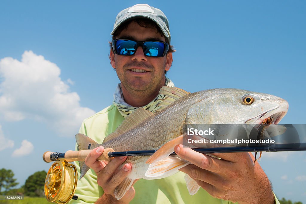 Fisherman holding fish and fly rod A fly fishing angler holding fish and fly rod with blue skys Charleston - South Carolina Stock Photo