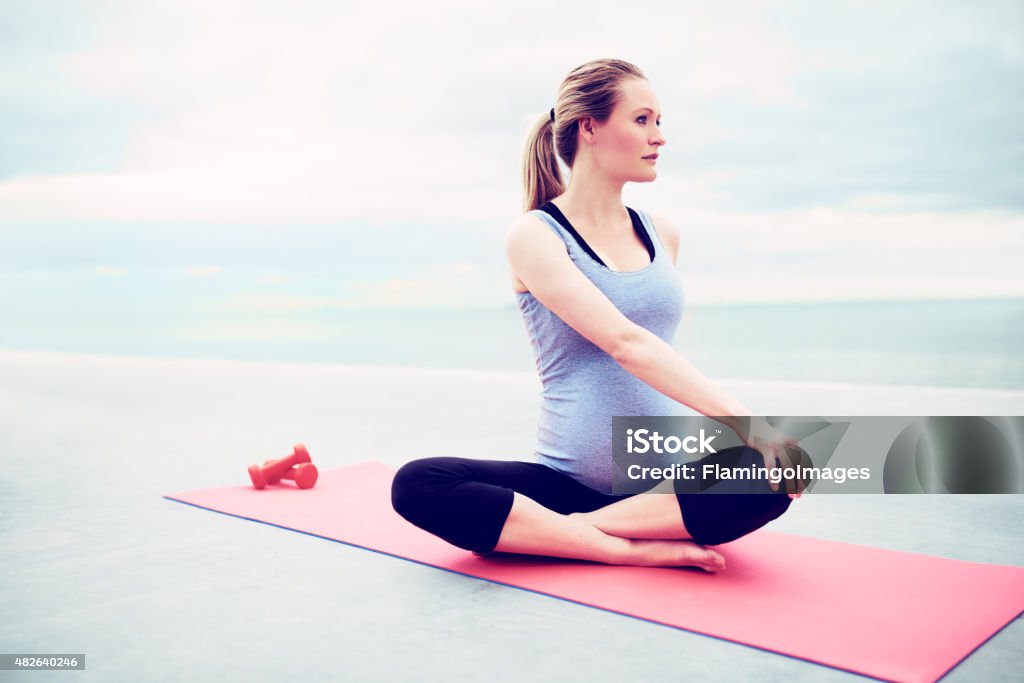Pregnant young woman doing fitness exercises Pregnant young woman doing fitness exercises sitting cross legged on a gym mat twisting her body to strengthen her stomach and back muscles Exercising Stock Photo