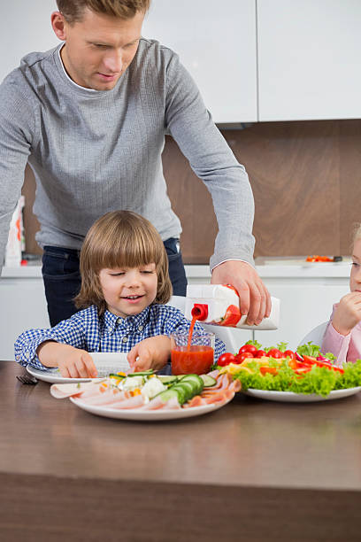 Father pouring juice for son at table in kitchen