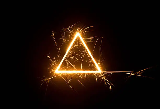 Bright burning triangle-shaped sparks on dark background with copy space.