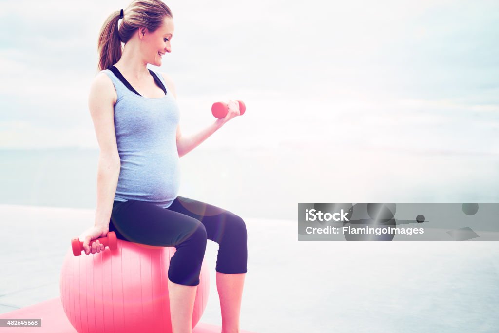 Pregnant woman doing fitness exercises Pregnant woman doing fitness exercises sitting on a pilates gym ball working out with dumbbells, profile view with copyspace 2015 Stock Photo