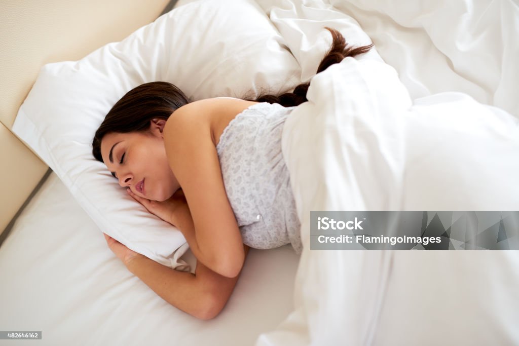 Young woman asleep on her side. Young woman asleep on her side under the white duvet. Braided Hair Stock Photo