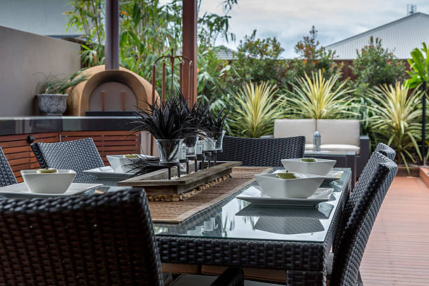 Patio dining table and chairs sitting outside in a leafy paved backyard of a contemporary home