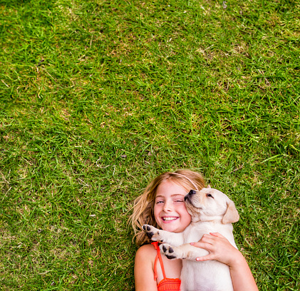 Happy girl holding labrador puppy lying on grass