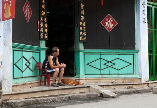 Hoi An, Vietnam - June 22, 2015: Unidentified old man sitting in front of his ancient house with his dog laying beside in Hoi An town, Quang Nam province. Hoi An is a World Heritage Site by UNESCO.