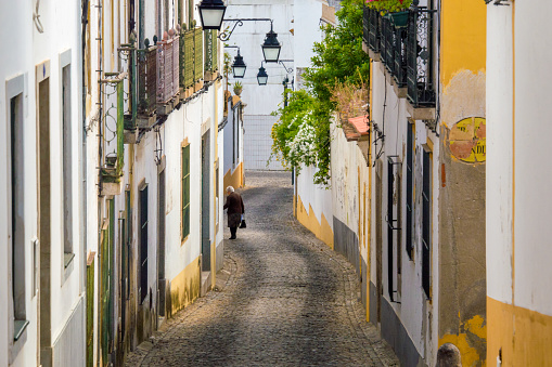 Evora, Portugal - May 2, 2013: Hilly street in Evora, Portugal.Along the street are many old houses, mainly in white and yellow colours. A woman is walking in the distance.  